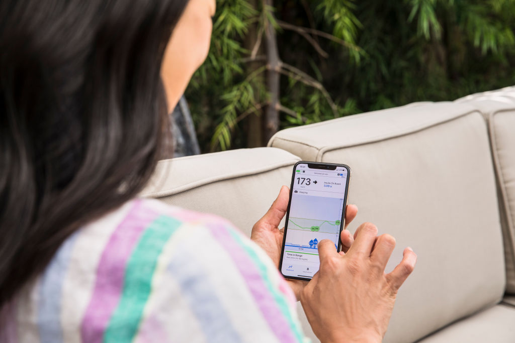 Close-up looking over shoulder of woman checking her diabetes management app on her smartphone.