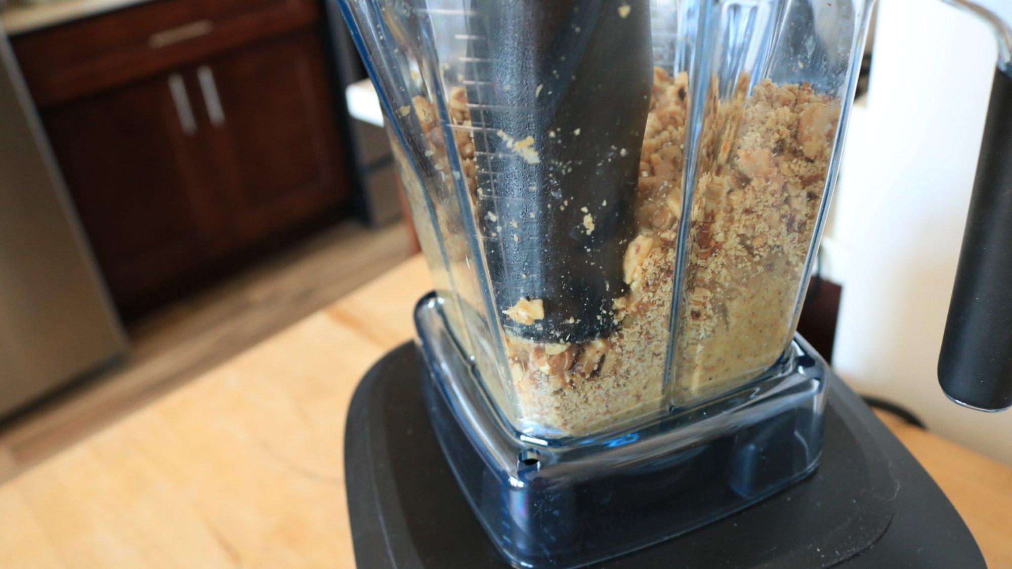 How to Make Peanut Butter in the Vitamix Ascent X5 4 A plastic tamper pressing nut bits in a blender.